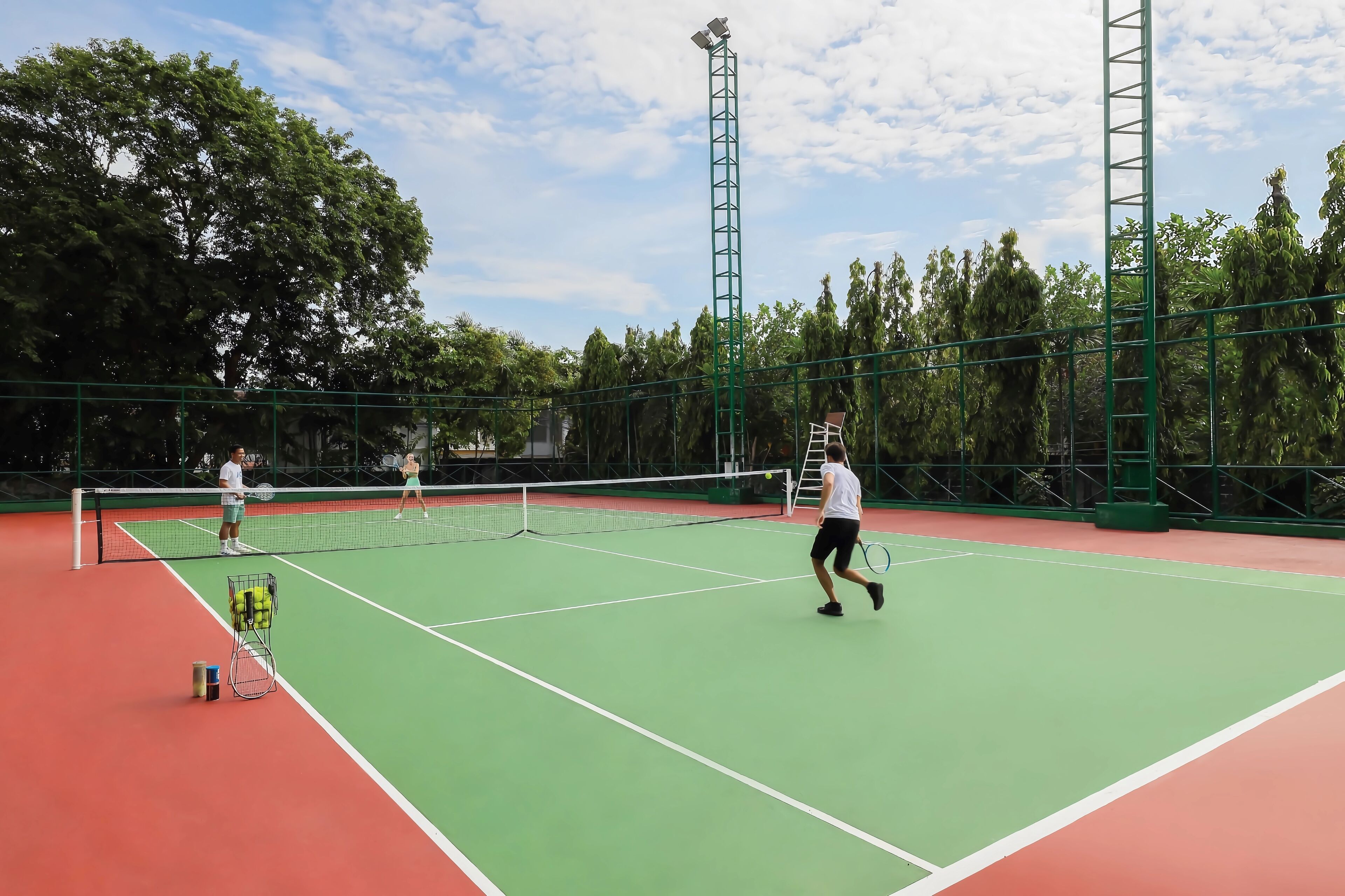 A tennis court with a net, two players, and a ball cart.
