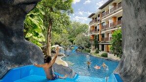 Zona de piscina con tobogán acuático, rodeada de exuberante vegetación y un edificio de varios pisos con balcones.