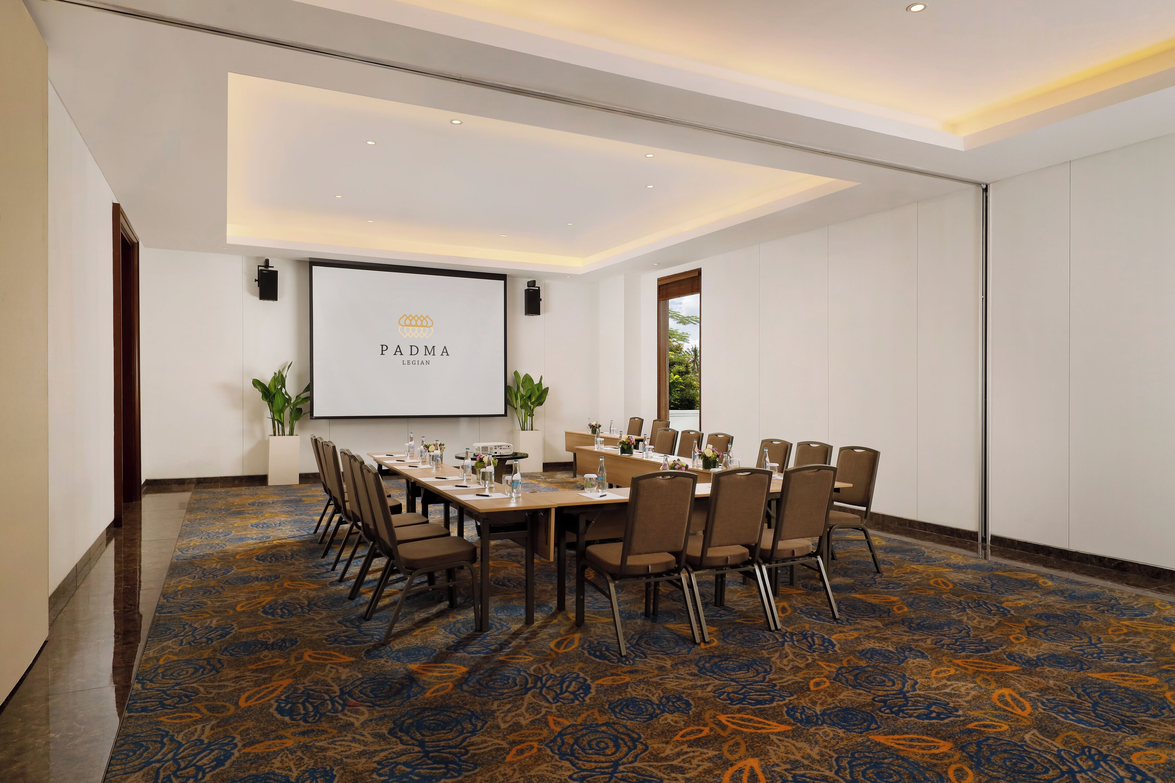 A conference room with a long table, chairs, a projector screen, and a carpeted floor.