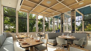 Un restaurante moderno con ventanas amplias, mesas de madera y asientos tapizados en gris.