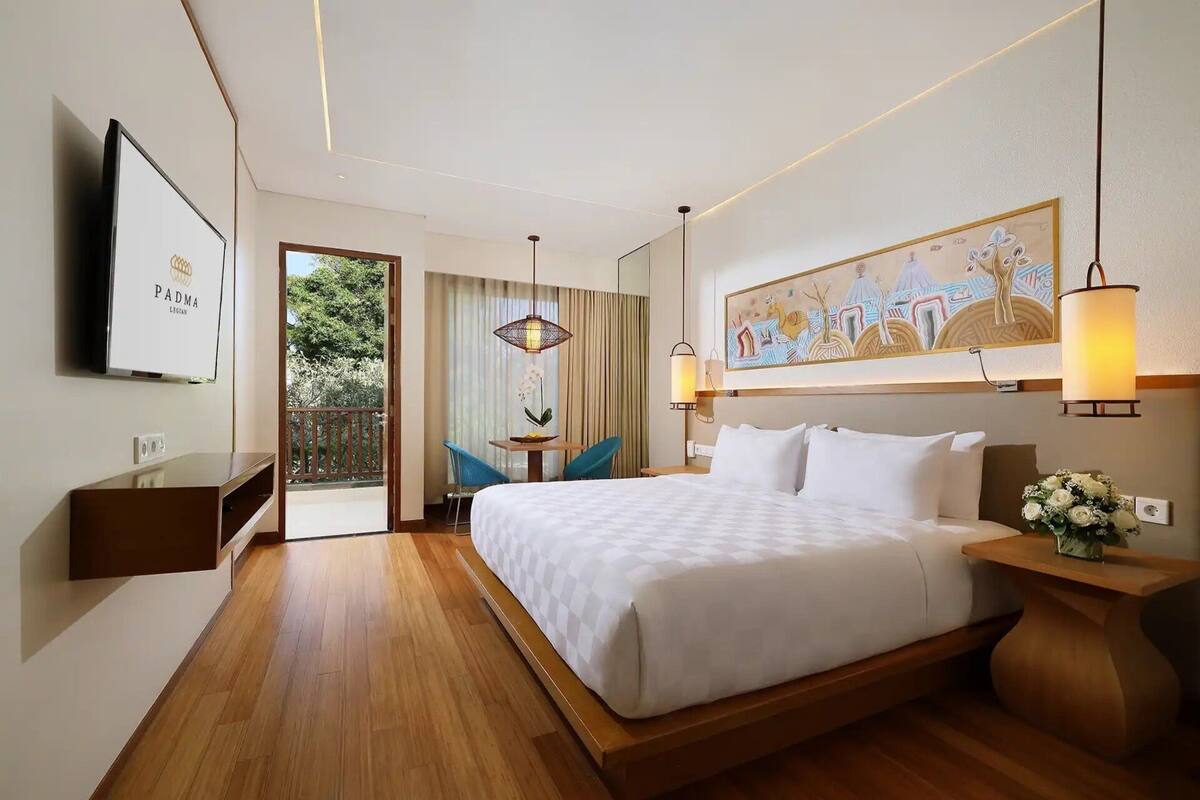 A hotel room with a large bed, a desk, a chair, a TV, and a painting on the wall.