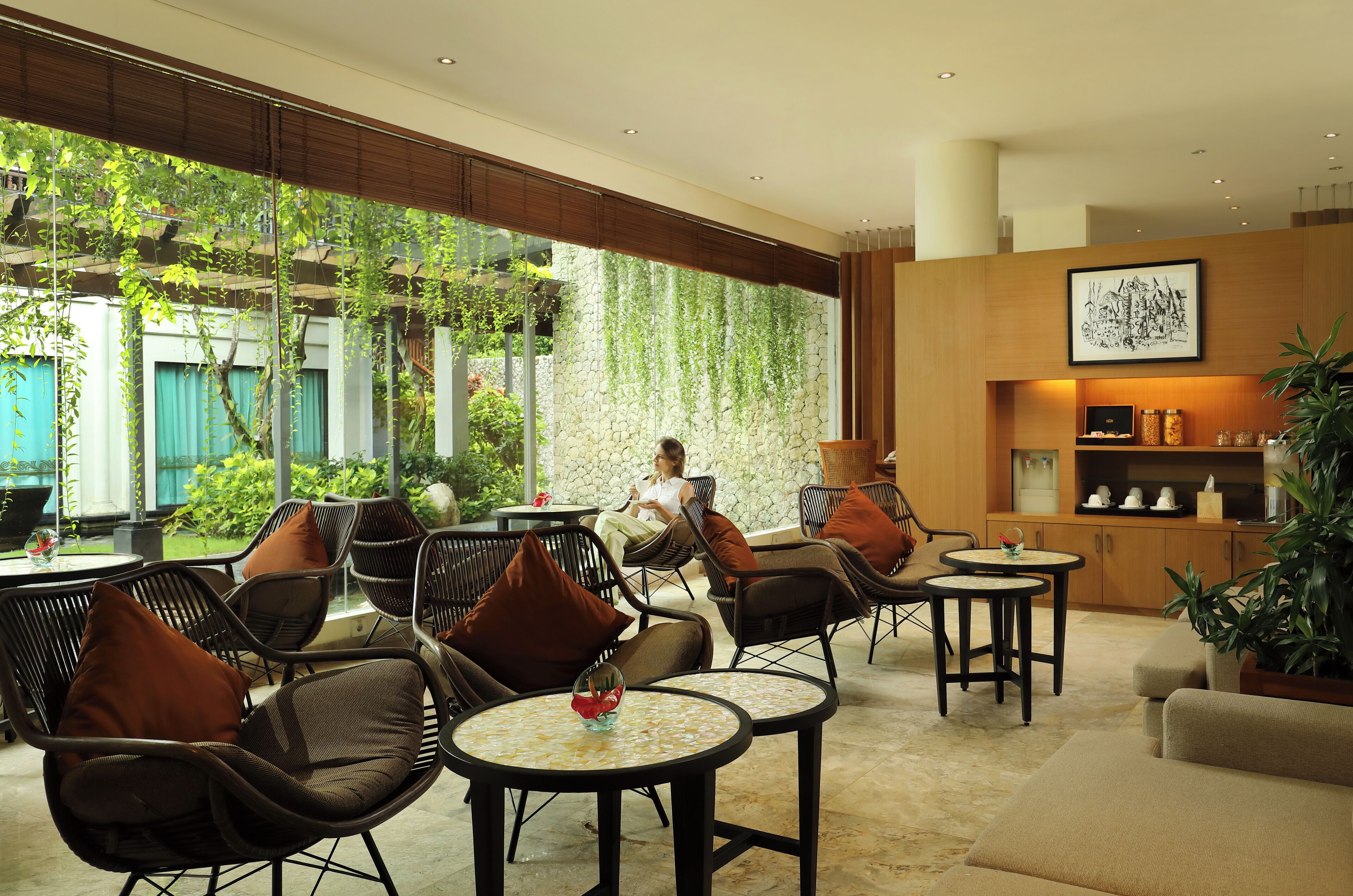 Un espacio lounge moderno con sillones de mimbre, mesas redondas y vistas al exterior.
