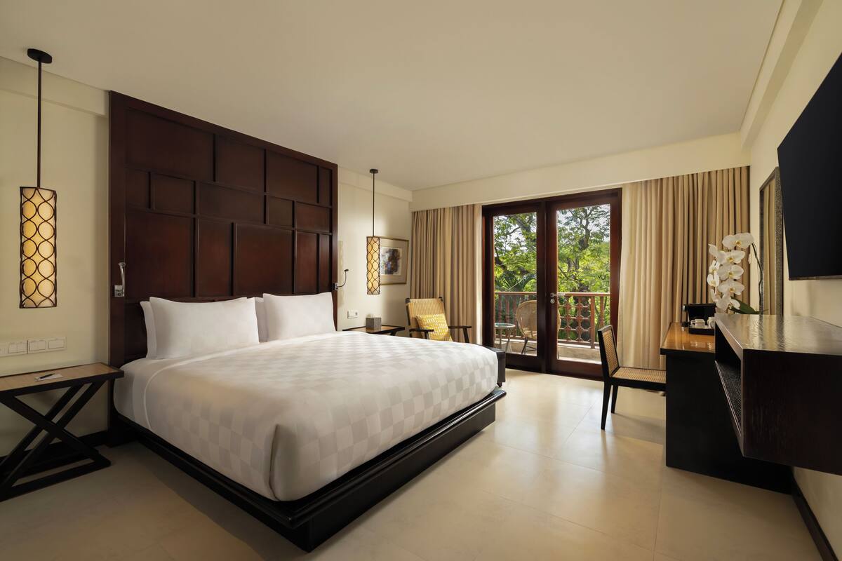 A modern hotel room with a large bed, a desk, and a balcony with curtains.