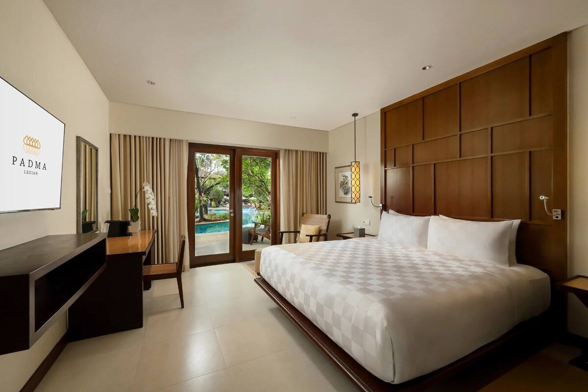 A hotel room with a large bed, a desk, a chair, a TV, and a view of an outdoor swimming pool.