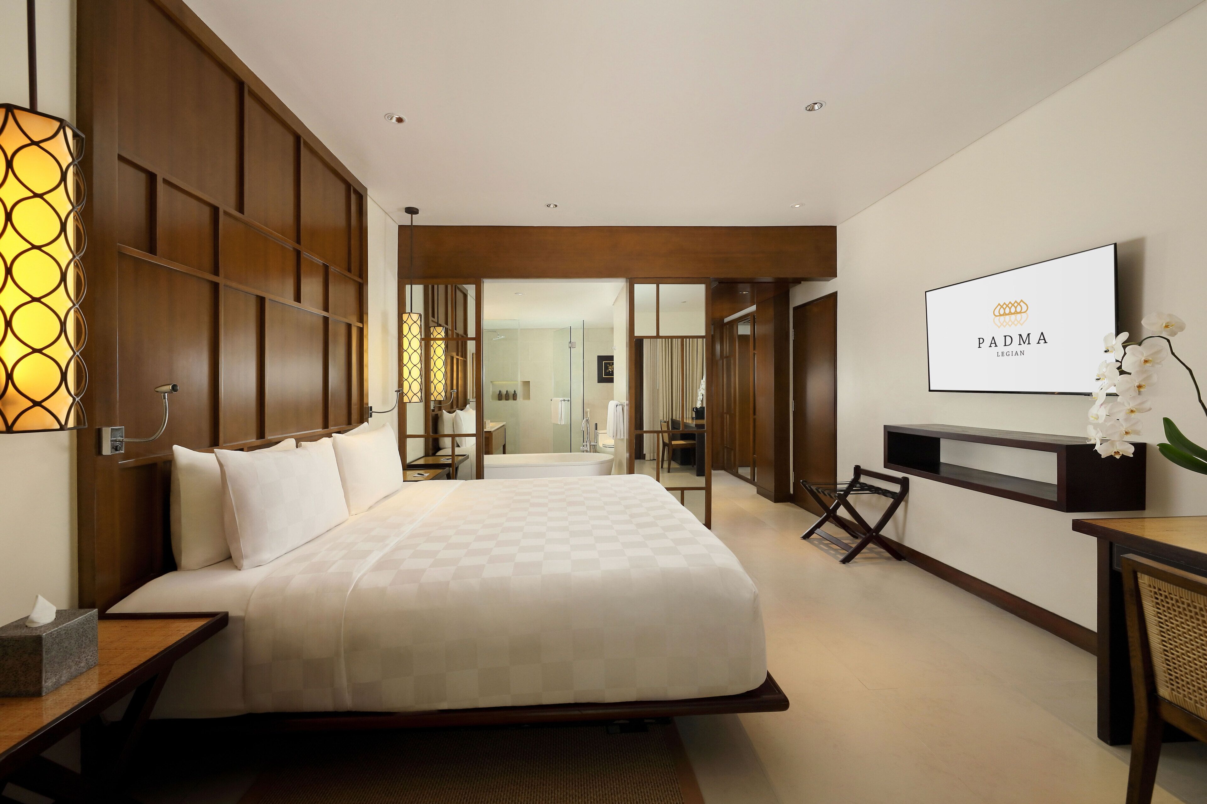 A hotel room with a large bed, a desk, a TV, and a bathroom visible through an open door.
