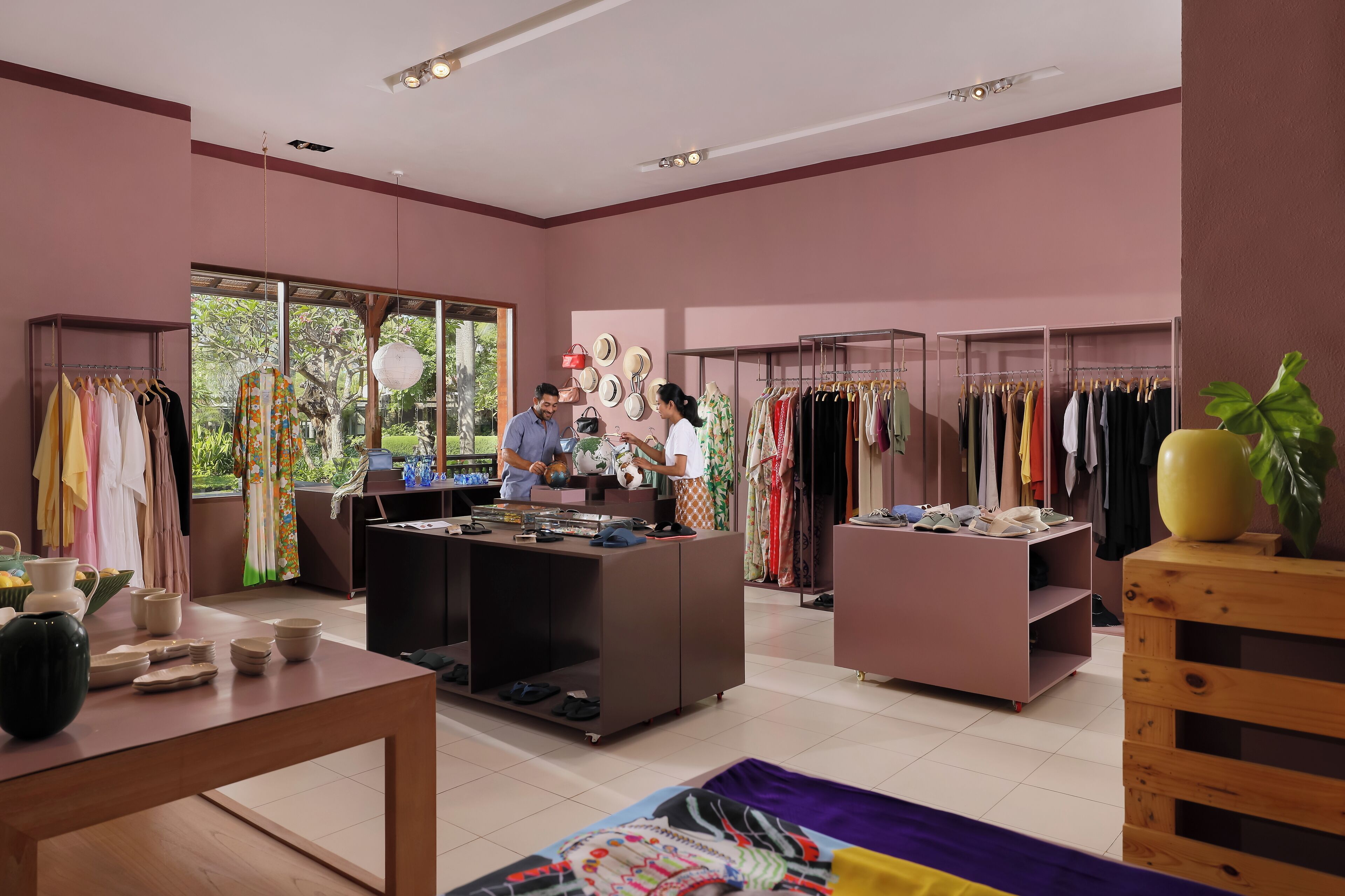 Habitación de un hotel boutique con un ventanal grande, un escritorio de madera y varios artículos de ropa exhibidos en perchas.