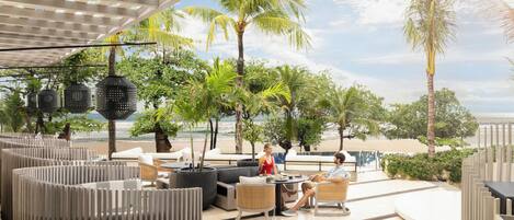 An outdoor seating area with a view of the beach, featuring modern furniture and potted plants.