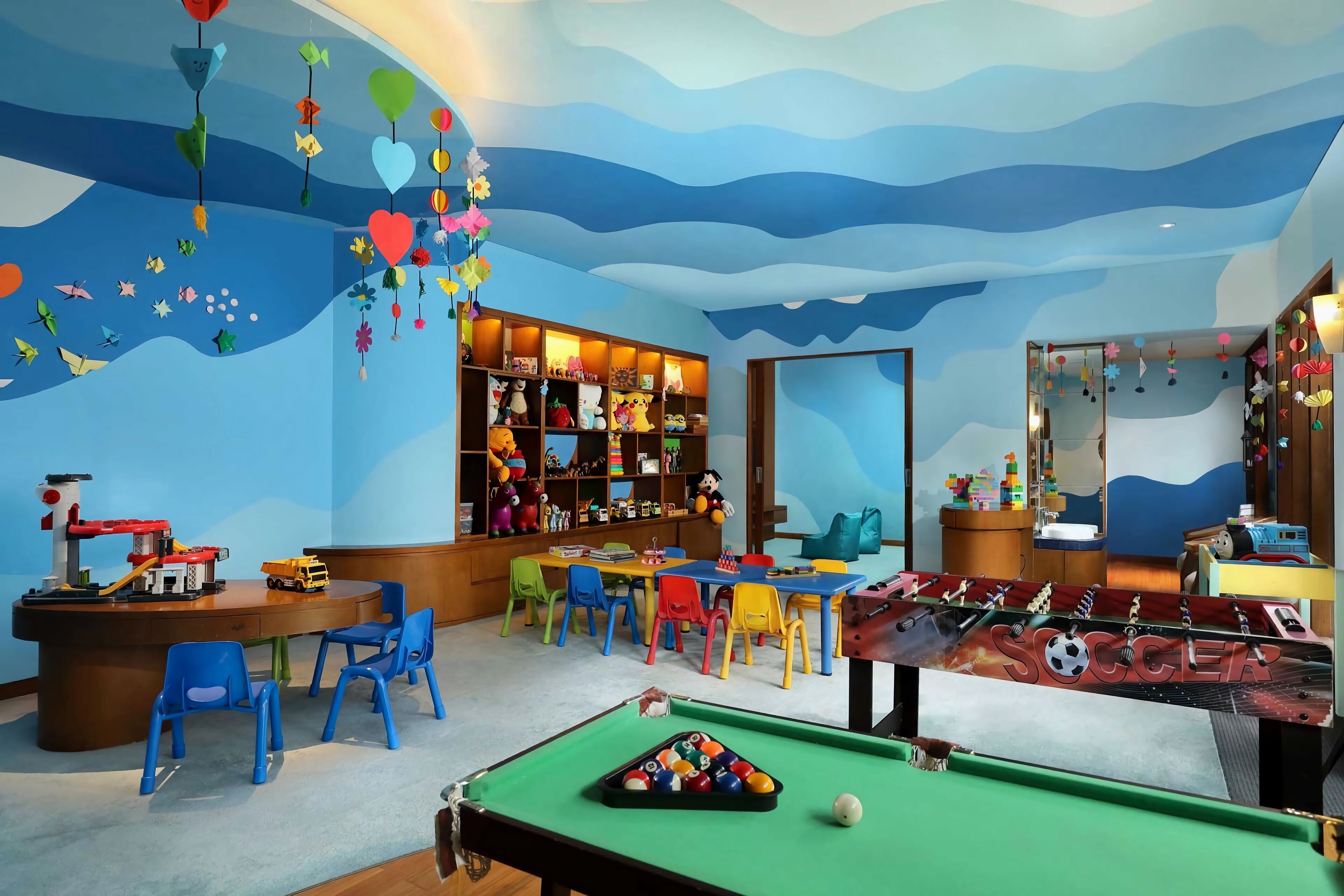 A children's playroom with a pool table, colorful chairs, and a toy collection.