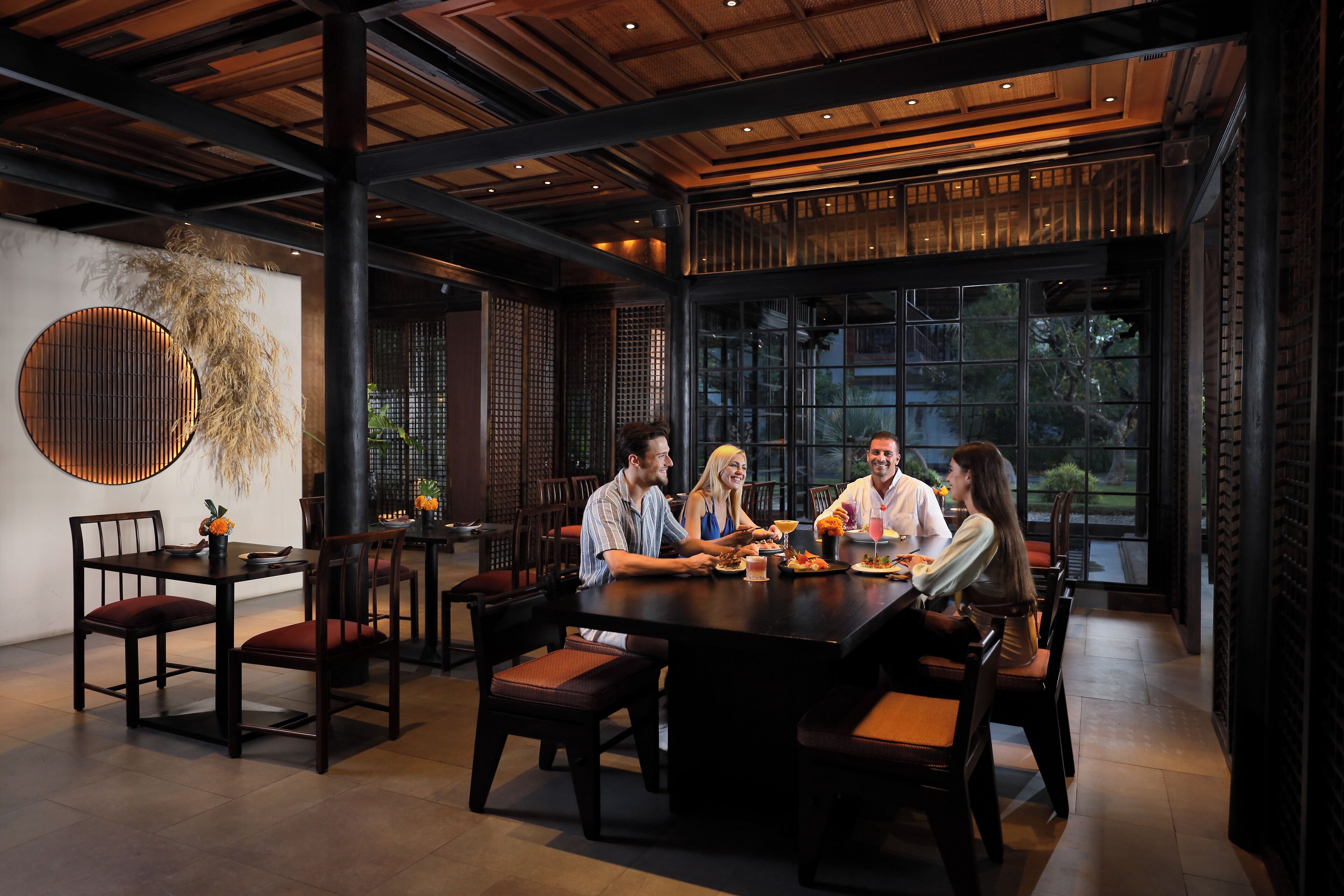 A modern dining area with a large table and chairs, surrounded by large windows and a decorative wall.