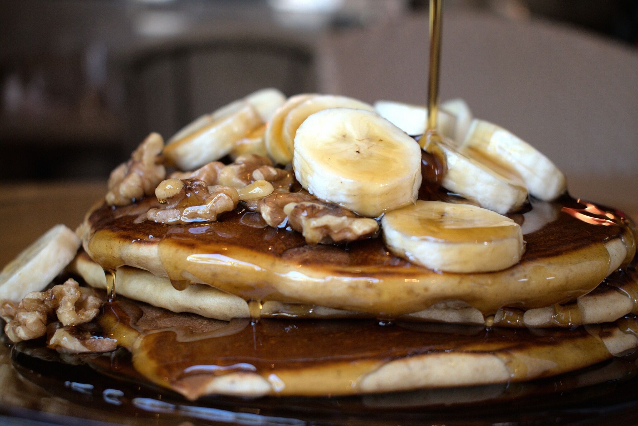 A stack of pancakes with banana slices and walnuts, topped with syrup.