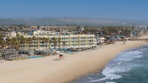 A beachfront hotel with multiple floors, a beach in the foreground, and palm trees lining the property. - Pier South Resort, Autograph Collection by Marriott (Imperial Beach)