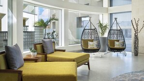 A spacious lobby with a yellow sofa, two hanging chairs, and a large potted plant. - Pier South Resort, Autograph Collection by Marriott (Imperial Beach)