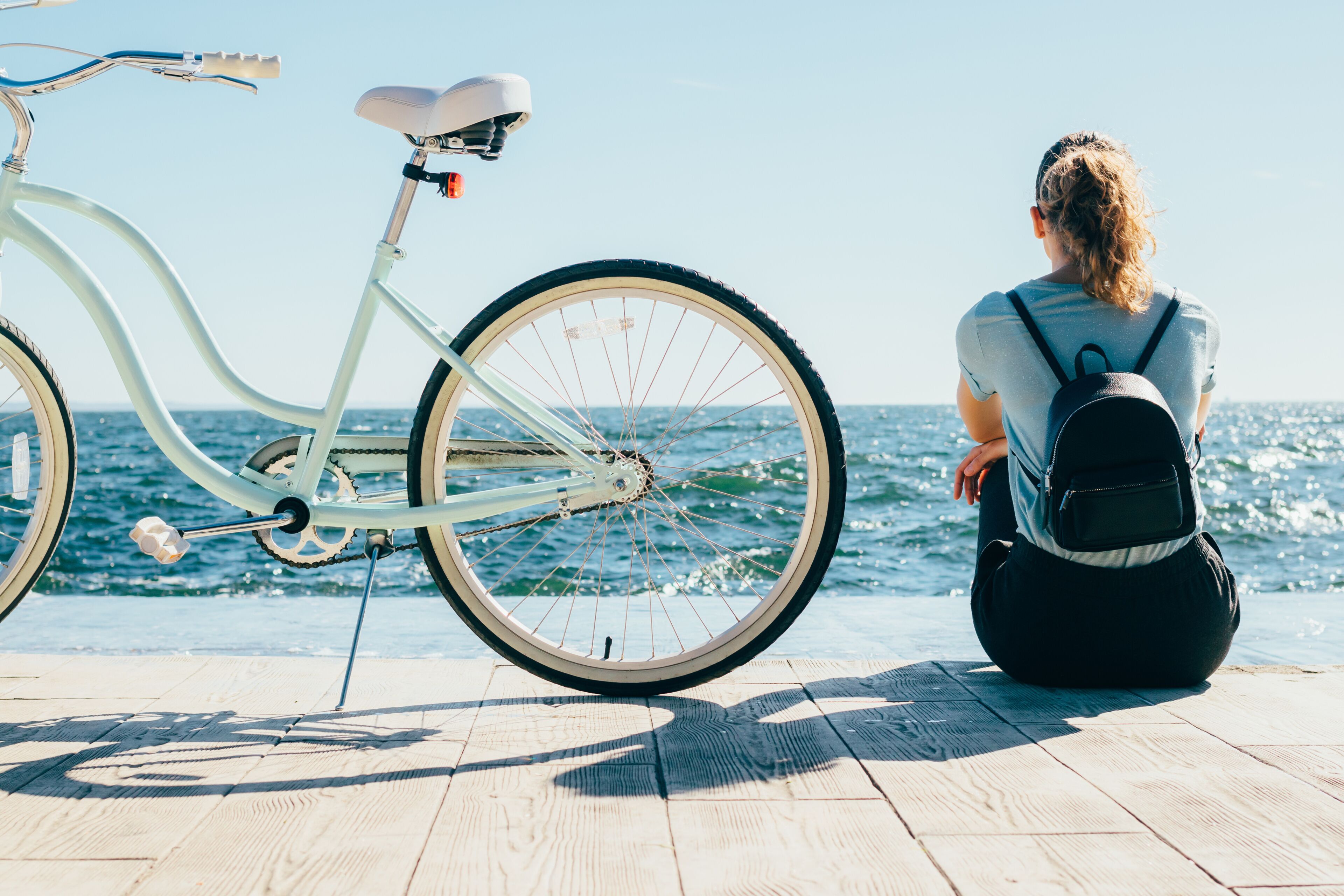 A person sitting by a white bicycle on a wooden deck by the sea.