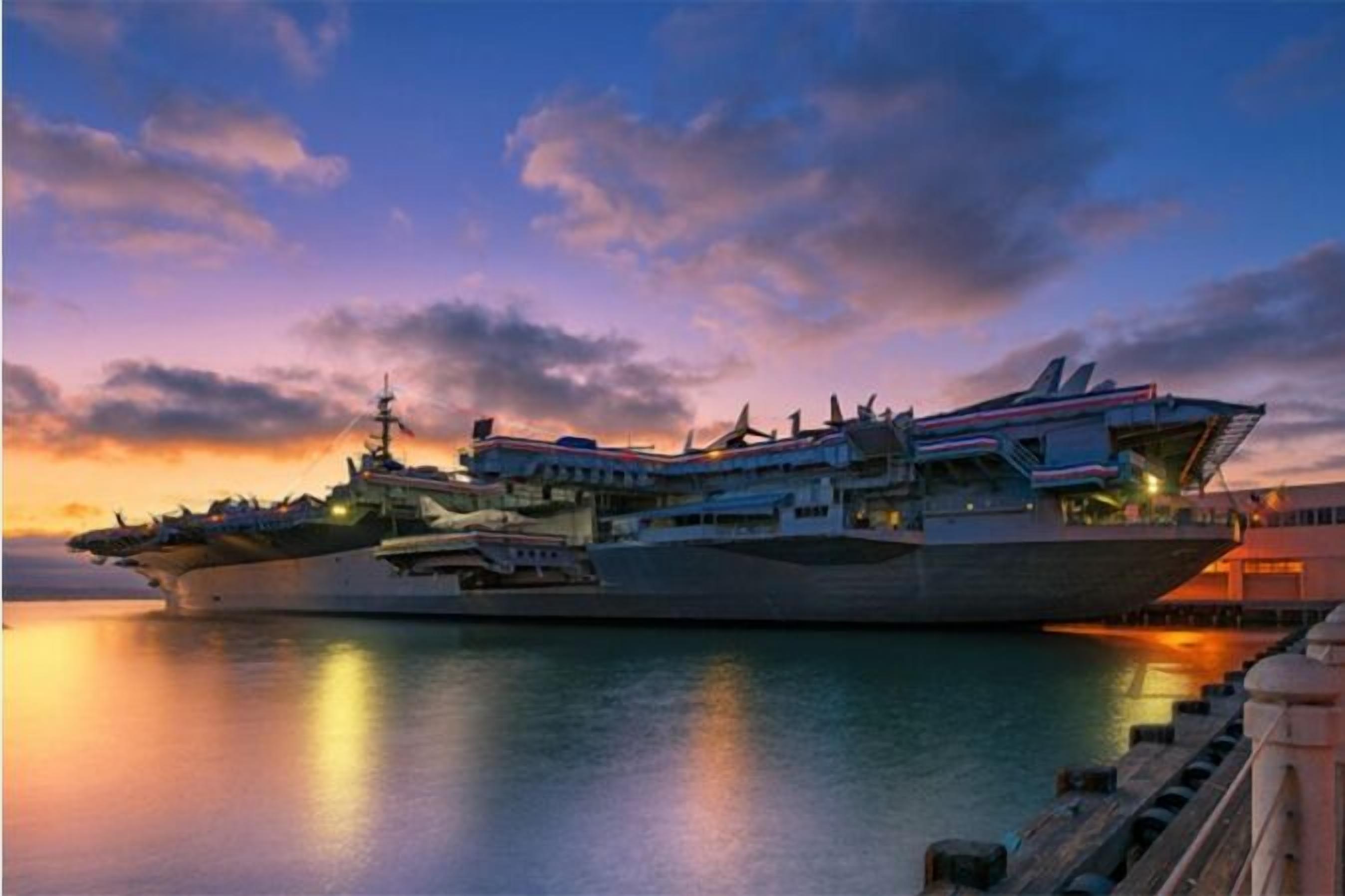 Un gran portaaviones atracado en un puerto con un atardecer de fondo.