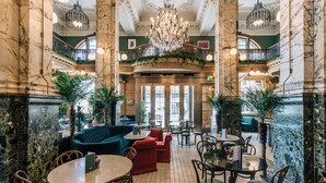 A grand lobby with marble columns, a large chandelier, and a red sofa.