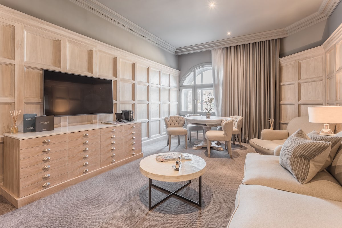 A spacious living room with a large TV, wooden cabinets, a round coffee table, and a comfortable seating area.