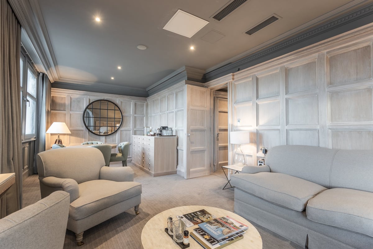 A spacious living room with a large sofa, a coffee table with magazines, and a kitchen area in the background.