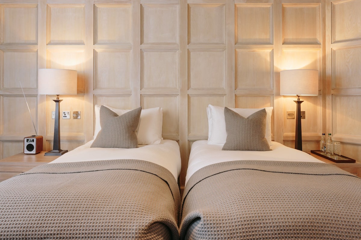 A hotel room with two beds, each with a lamp, a radio, and a nightstand.
