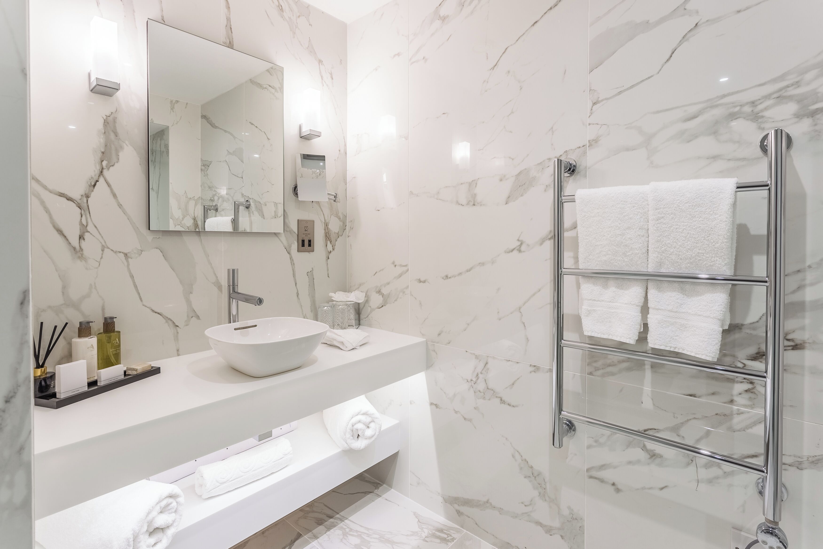 A modern bathroom with a marble backsplash, a large mirror, a white sink, and a glass shower enclosure.
