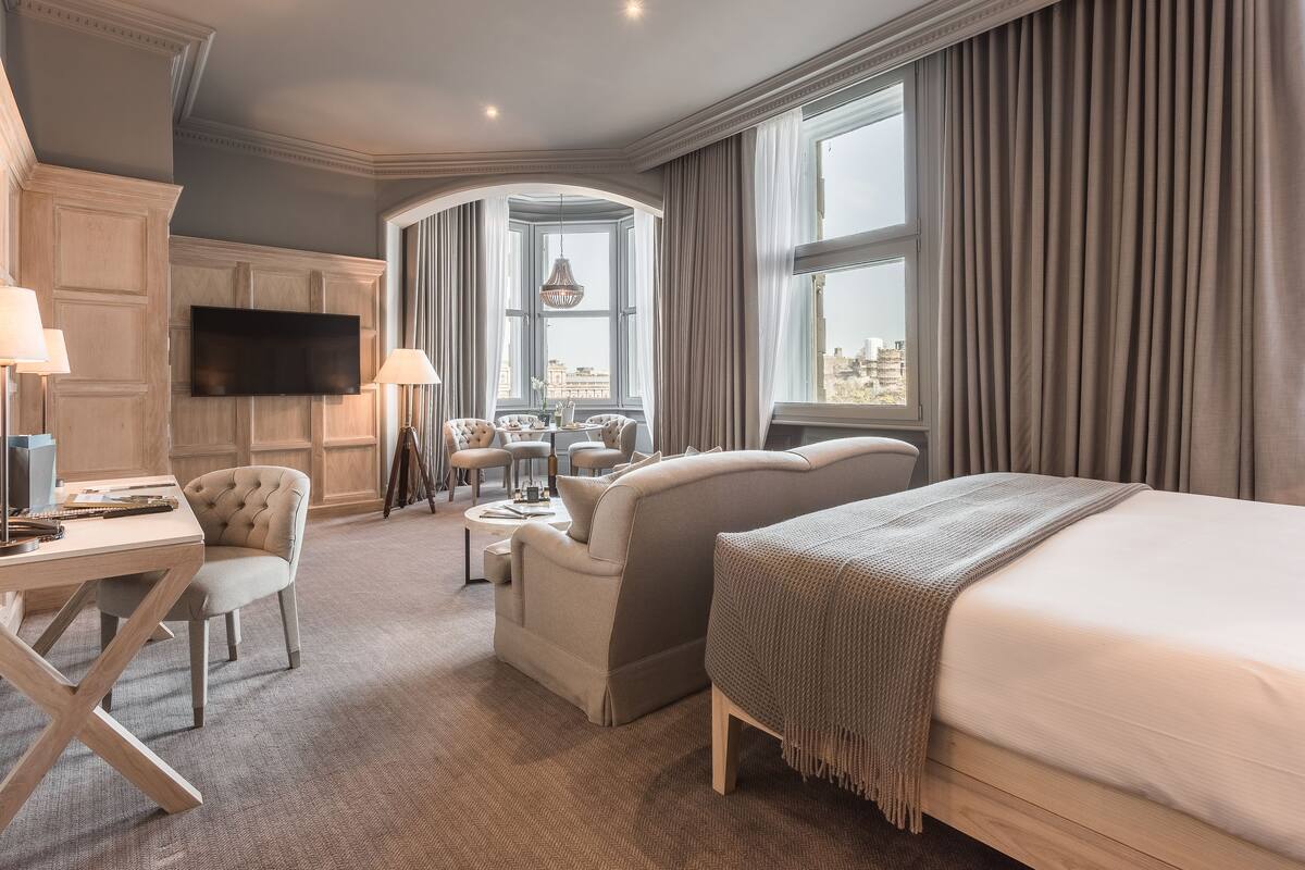 A hotel room with a bed, a desk, a chair, a sofa, and a TV.