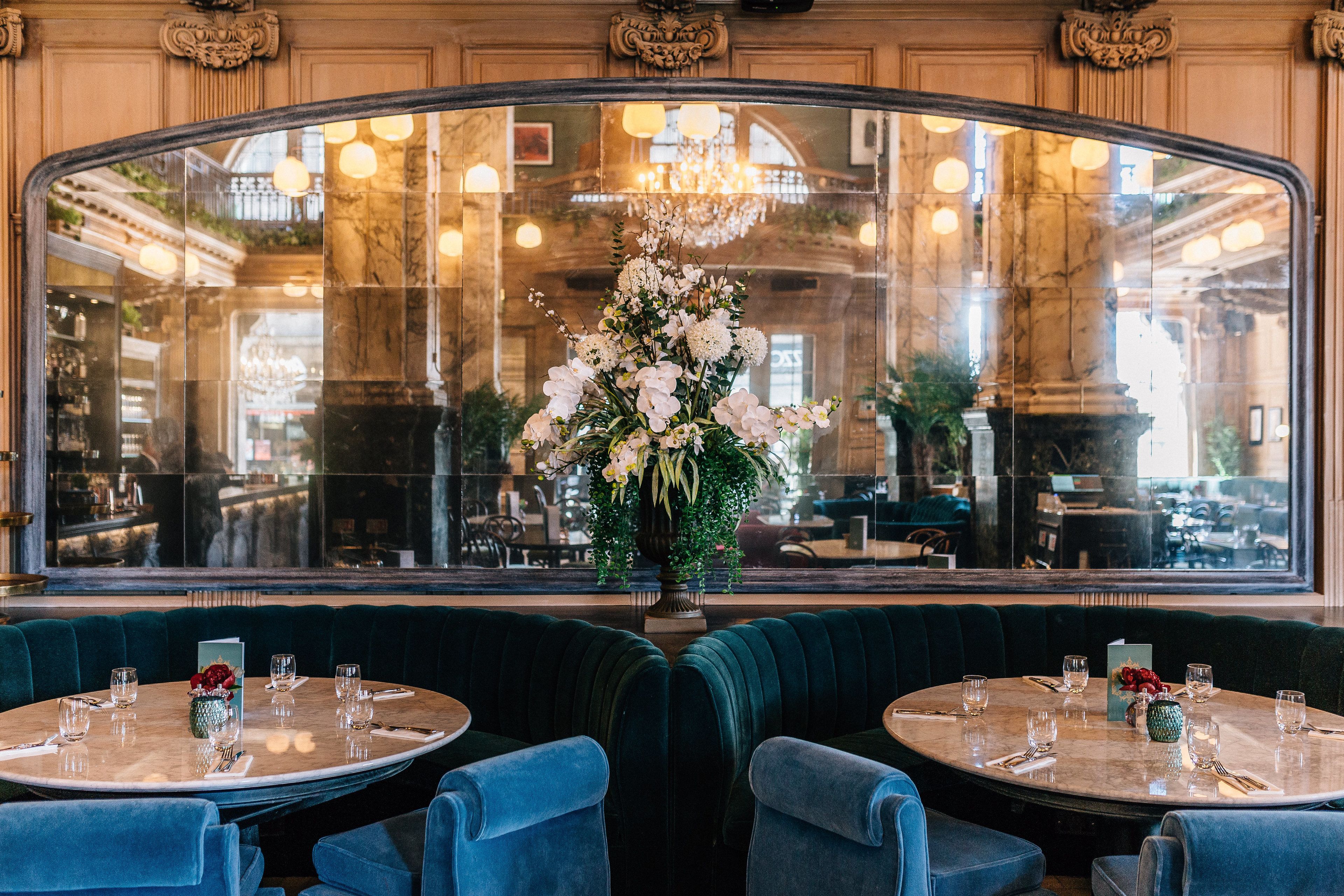 A restaurant with round tables, blue upholstered booths, and a large window with a view of the interior.
