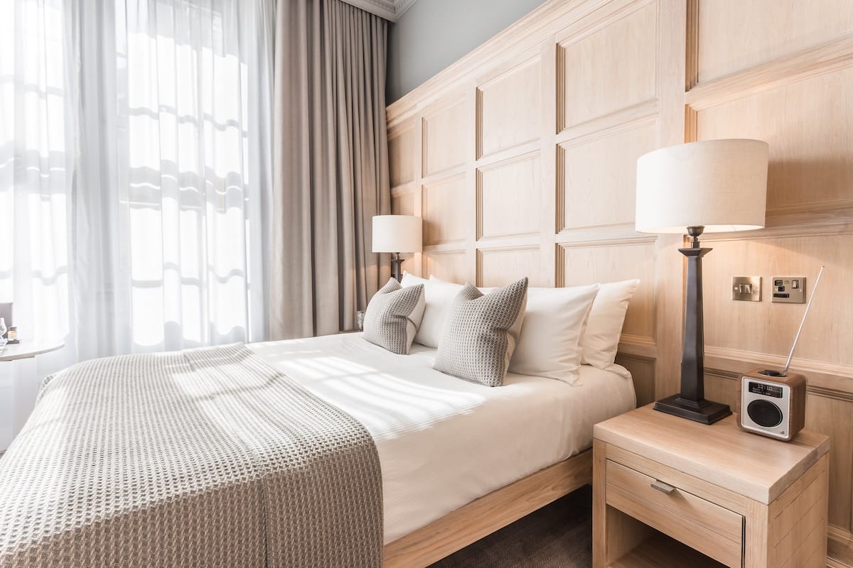 A hotel room with a large bed, two bedside lamps, a radio, and a wooden headboard.