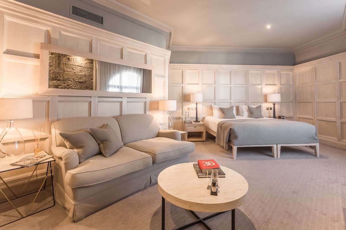 A hotel room with a large bed, a sofa, a round coffee table, and a nightstand.