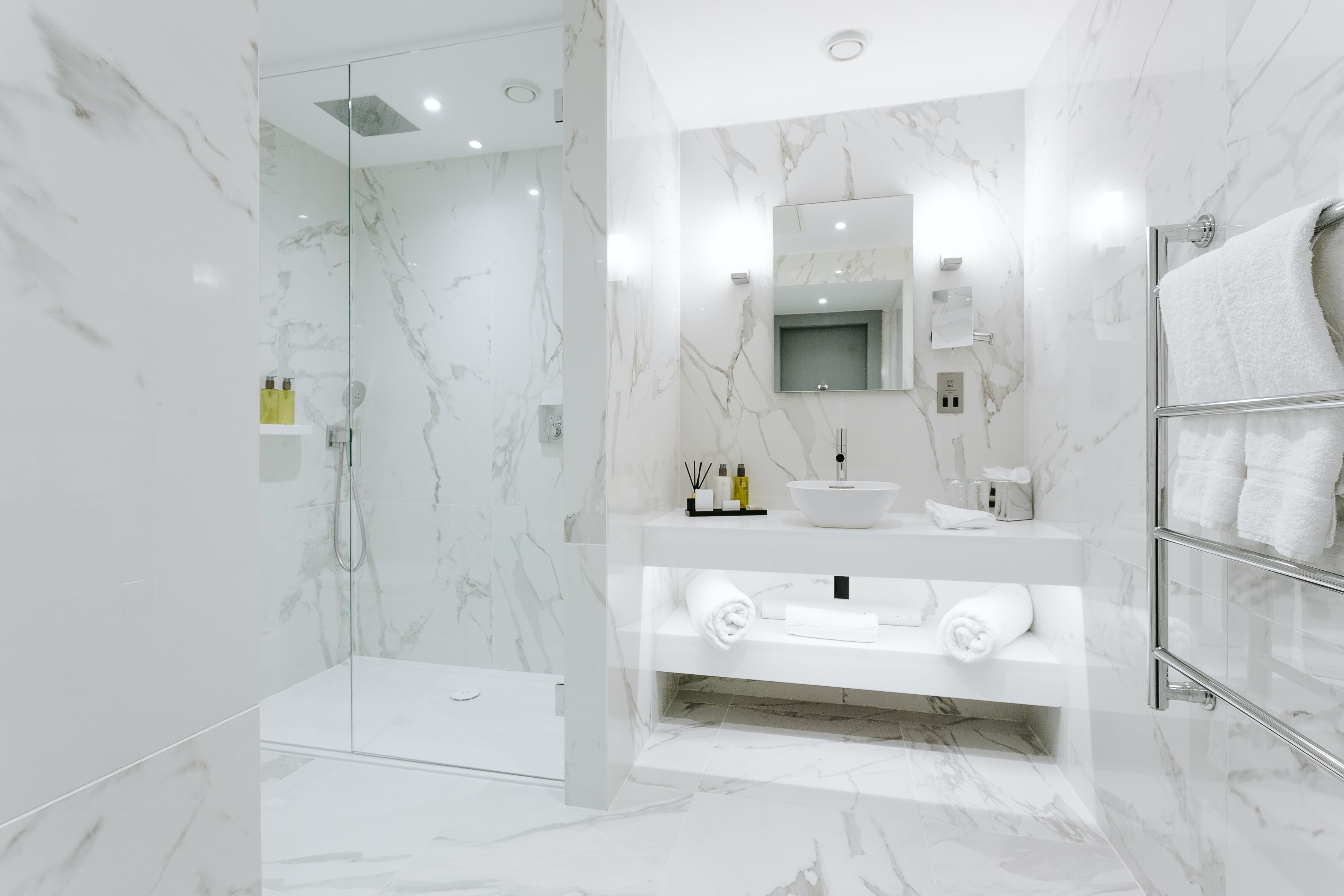 Un bany modern amb dutxa de vidre, un lavabo de marbre blanc i un suport per a tovalloles.