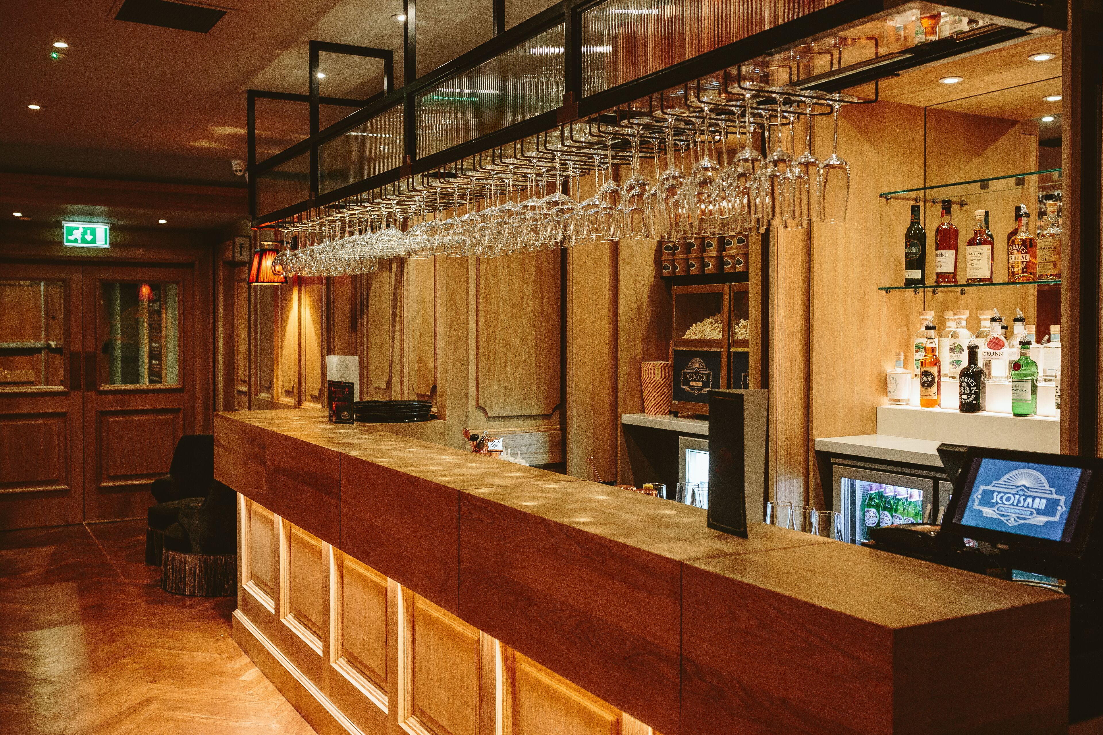 A bar area with wooden paneling, a counter with a cash register, and shelves stocked with bottles.