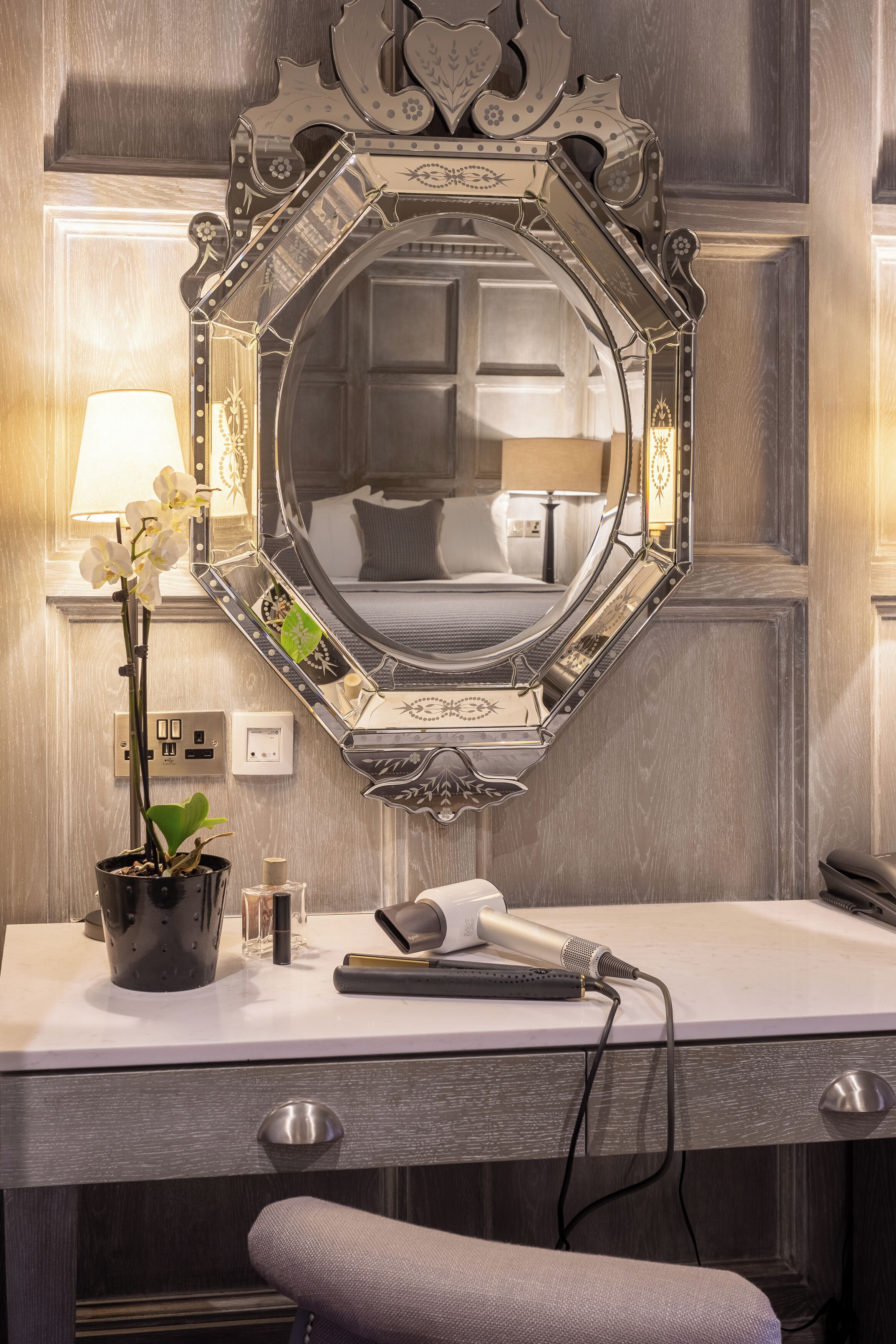 A bathroom vanity with a large mirror, a potted orchid, and a hairdryer on the counter.