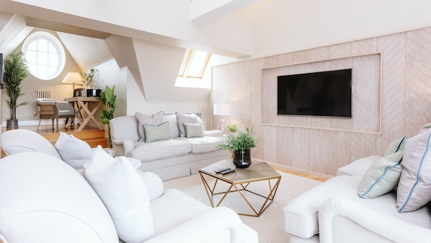 A modern living room with a white sofa, a coffee table, and a TV mounted on the wall.