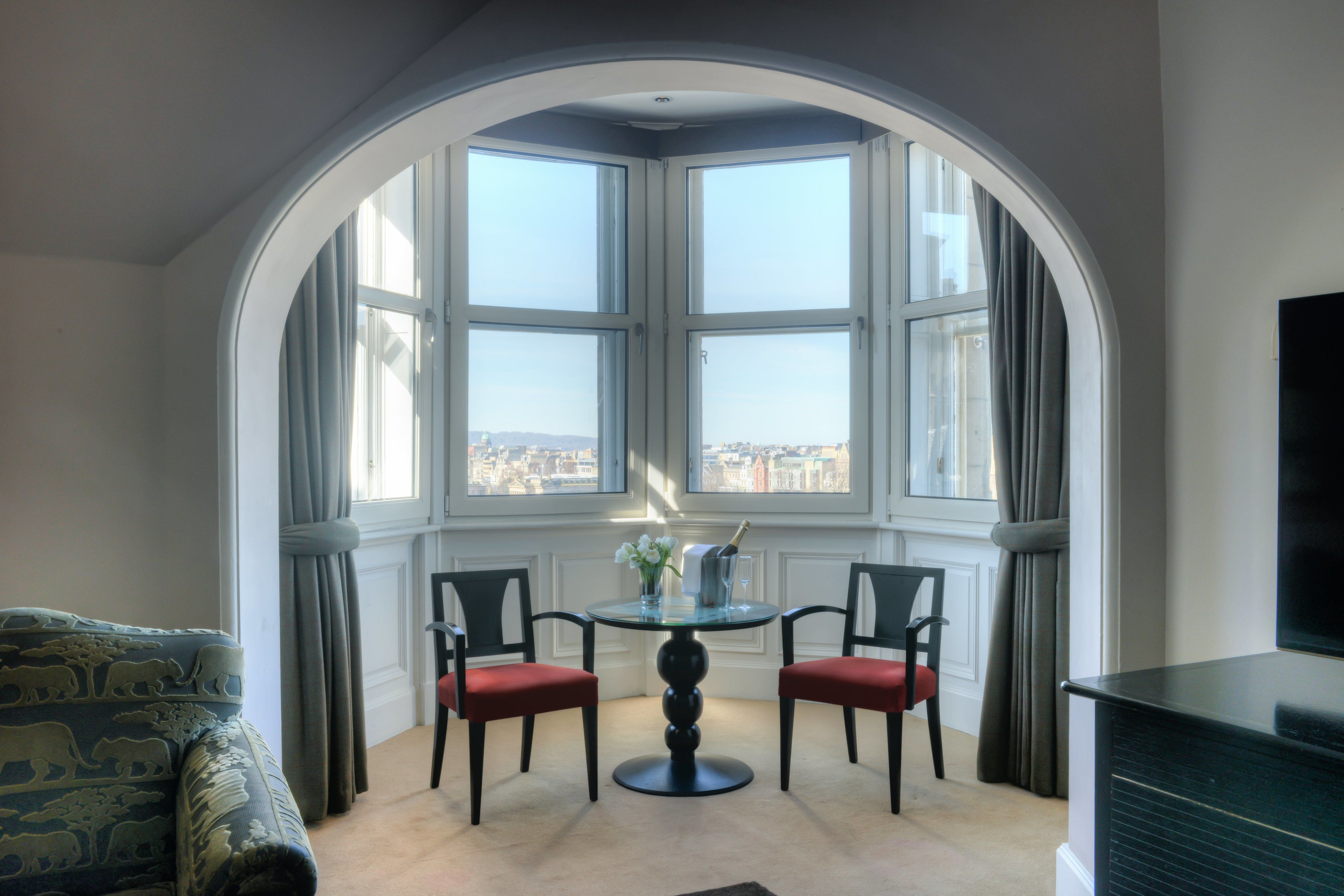 Een kamer met een erker, een ronde tafel met twee stoelen, een bank en een televisie.