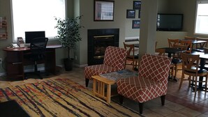 A living room with a fireplace, a television, and a dining area with chairs. - Grand Forks Inn (Grand Forks)