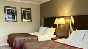 A hotel room with two beds, each with a grey and red patterned bedspread, a wooden headboard, a bedside lamp, and two framed botanical prints on the wall. - Grand Forks Inn (Grand Forks)