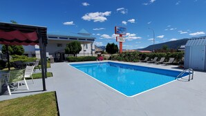 A swimming pool with a blue border, surrounded by lounge chairs and a covered seating area. - Grand Forks Inn (Grand Forks)
