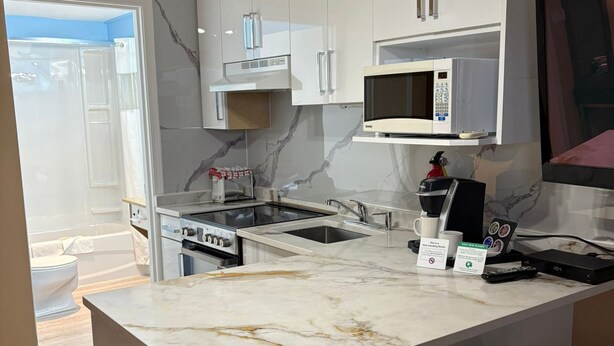 A modern kitchen with white cabinets, a marble countertop, a built-in microwave, and a coffee maker. - Grand Forks Inn (Grand Forks)