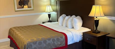 Una cama bien hecha con una colcha estampada, dos lámparas de noche, una mesita de noche con cajón y un cuadro en la pared.