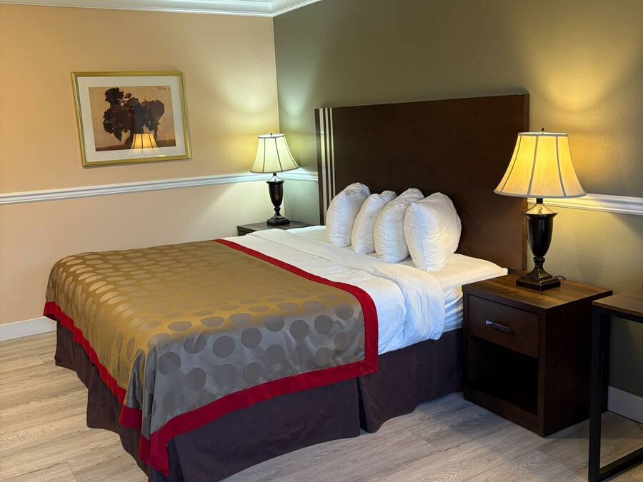 A neatly made bed with a patterned bedspread, two bedside lamps, a nightstand with a drawer, and a framed picture on the wall.