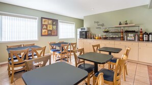 A dining area with wooden tables and chairs, a kitchen area with a microwave and a coffee station, and a wall with a positive message. - Grand Forks Inn (Grand Forks)