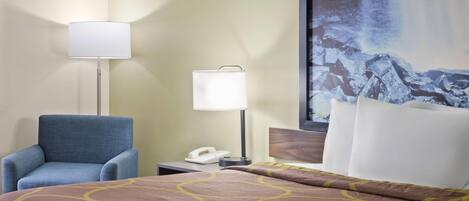 A hotel room with a bed, a blue armchair, a nightstand with a lamp, and a large painting of a waterfall.