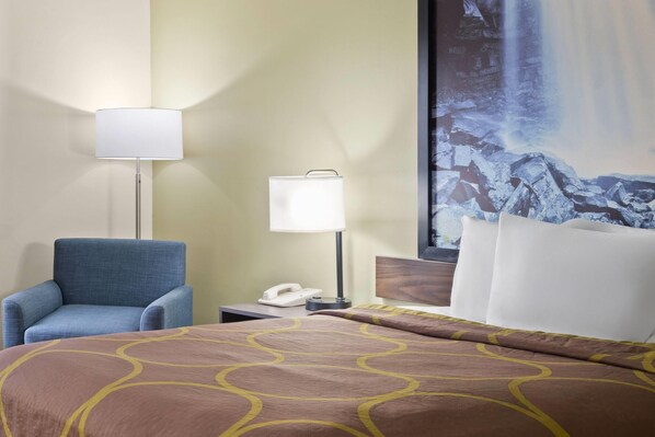 A hotel room with a bed, a blue armchair, a nightstand with a lamp, and a large painting of a waterfall. - Super 8 by Wyndham Hagerstown I-70 (Hagerstown)