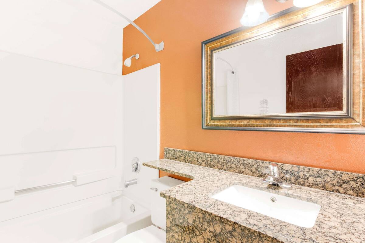 A bathroom with a white bathtub, a granite countertop sink, and a large mirror with a gold frame.