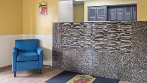 A reception area with a blue armchair, a wall-mounted sign, and a patterned wall. - Super 8 by Wyndham Hagerstown I-70 (Hagerstown)