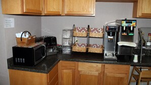 Una cocina con armarios de madera, microondas, cafetera y dispensador de bebidas.