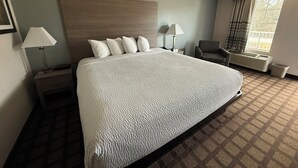 Een hotelkamer met een groot bed, twee nachtkastjes, een stoel, een raam met gordijnen en een radiator.