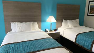 Two single beds with white bedding and a teal-patterned throw, set against a blue accent wall and a wooden headboard.