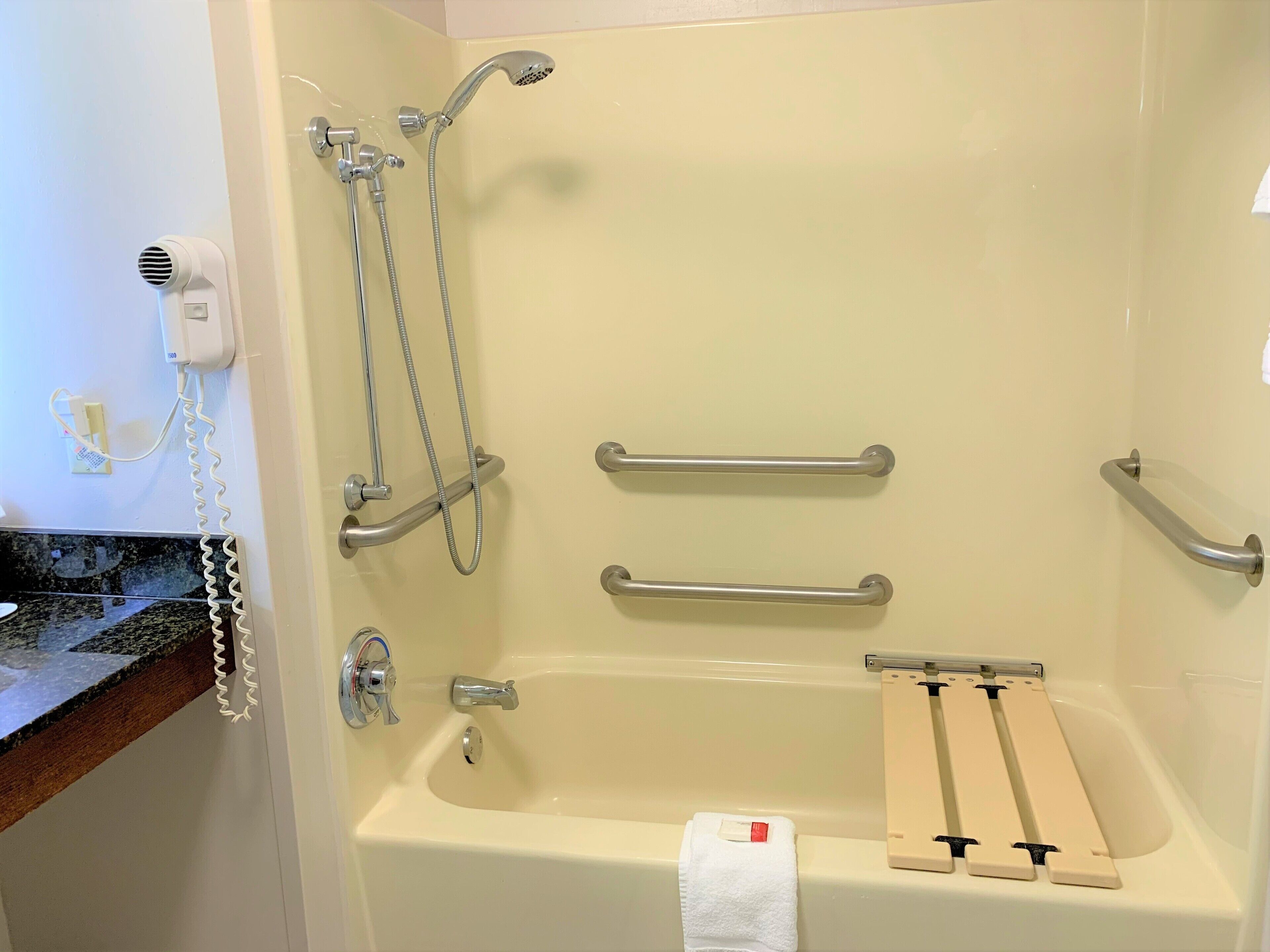 A bathroom with a bathtub, grab bars, a handheld showerhead, and a towel rack.