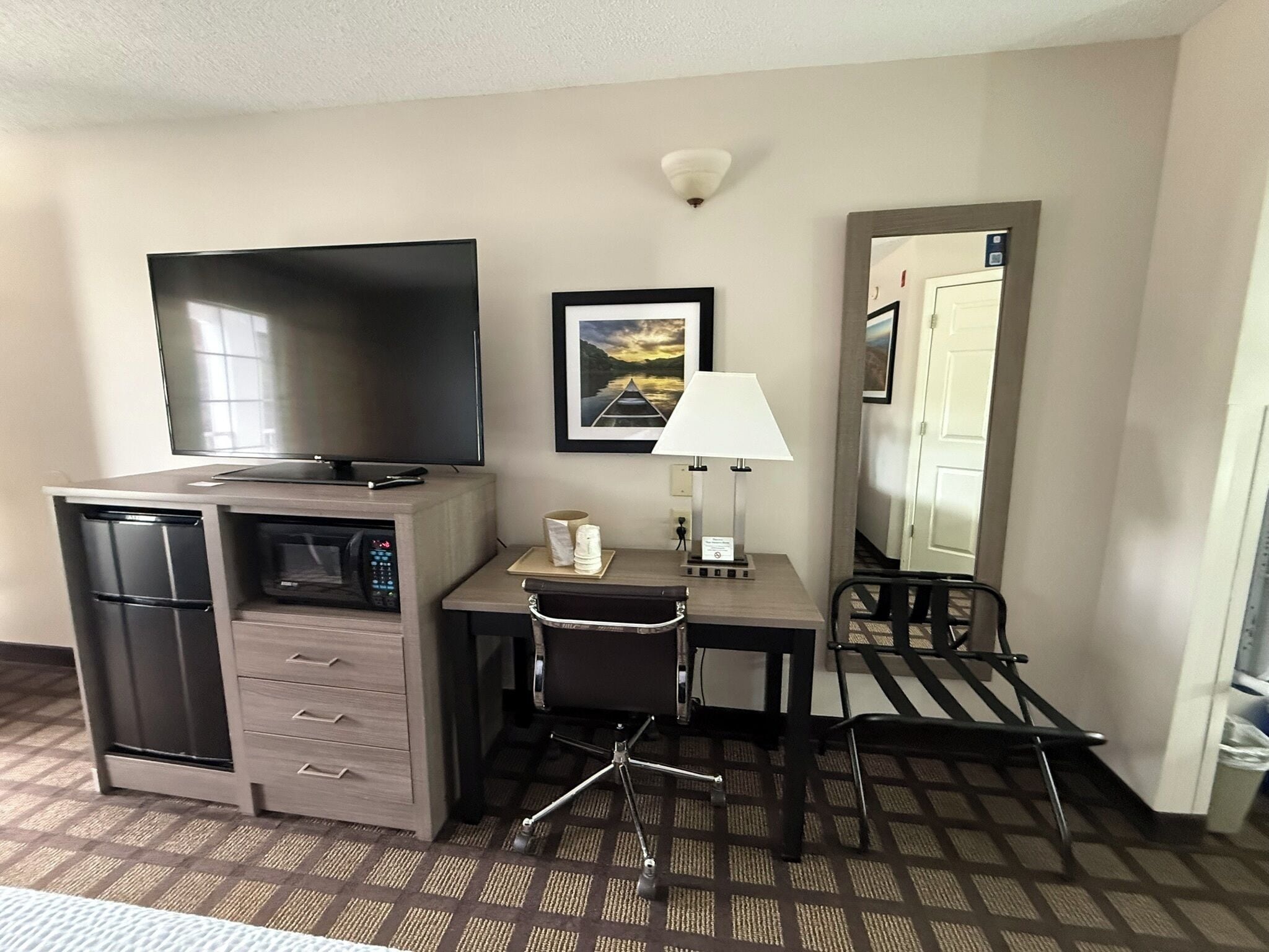 Habitación de hotel con escritorio, silla, televisor, microondas y un espejo grande.