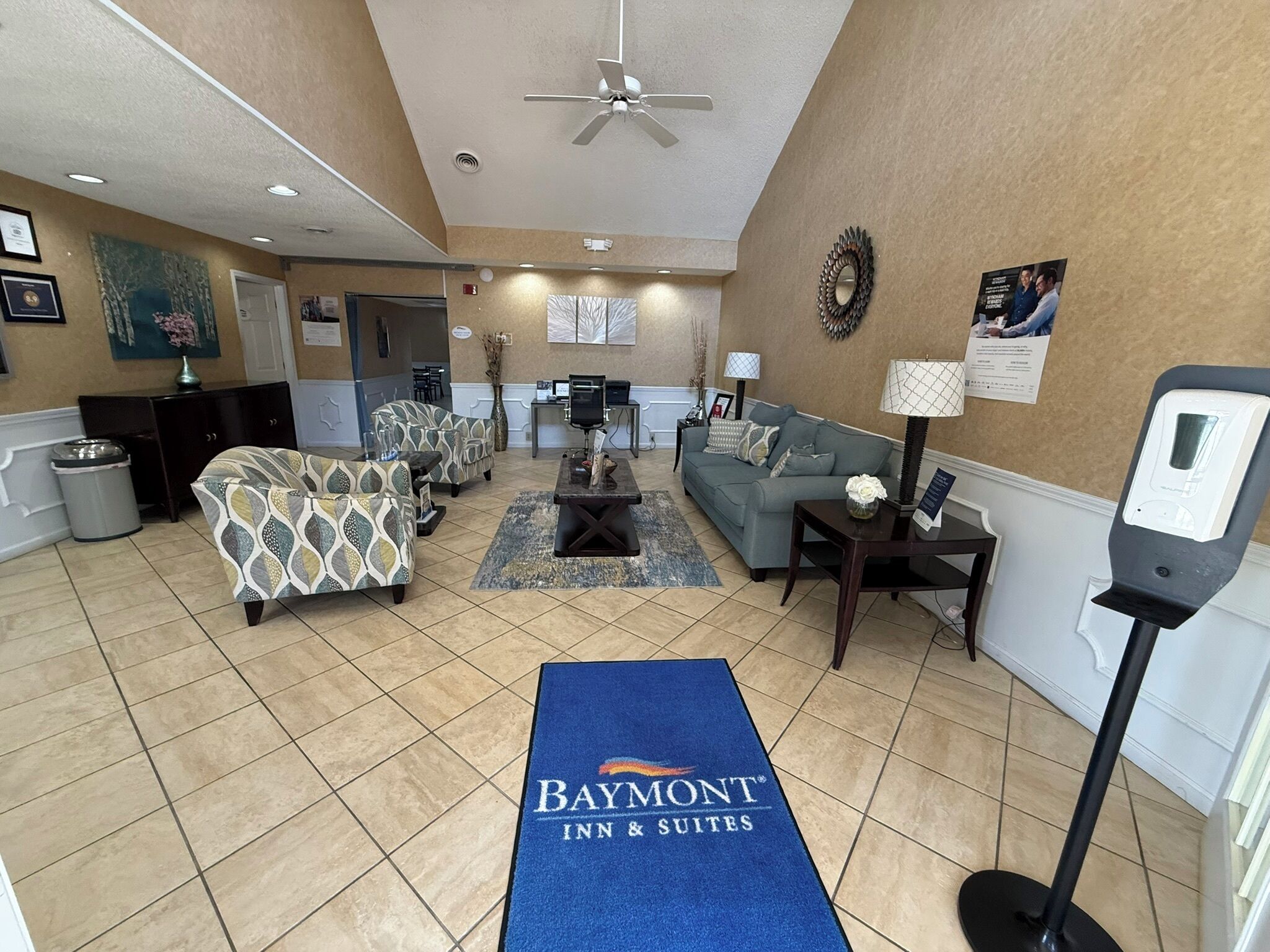 A hotel lobby with seating areas, a reception desk, and a Baymont Inn & Suites sign.