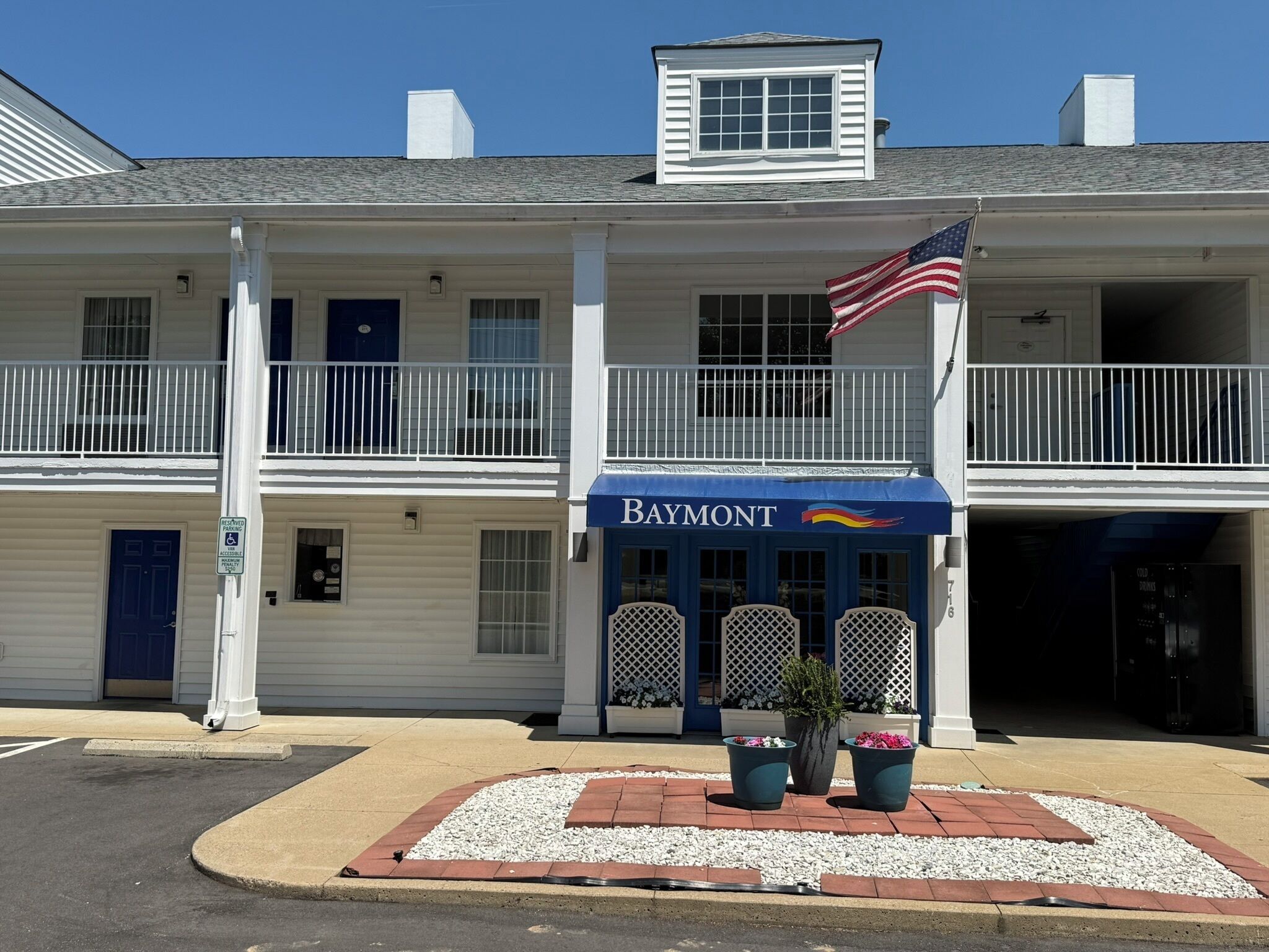 Un bâtiment à deux étages avec un auvent bleu portant l’inscription « Baymont », un drapeau et un panneau indiquant un parking.